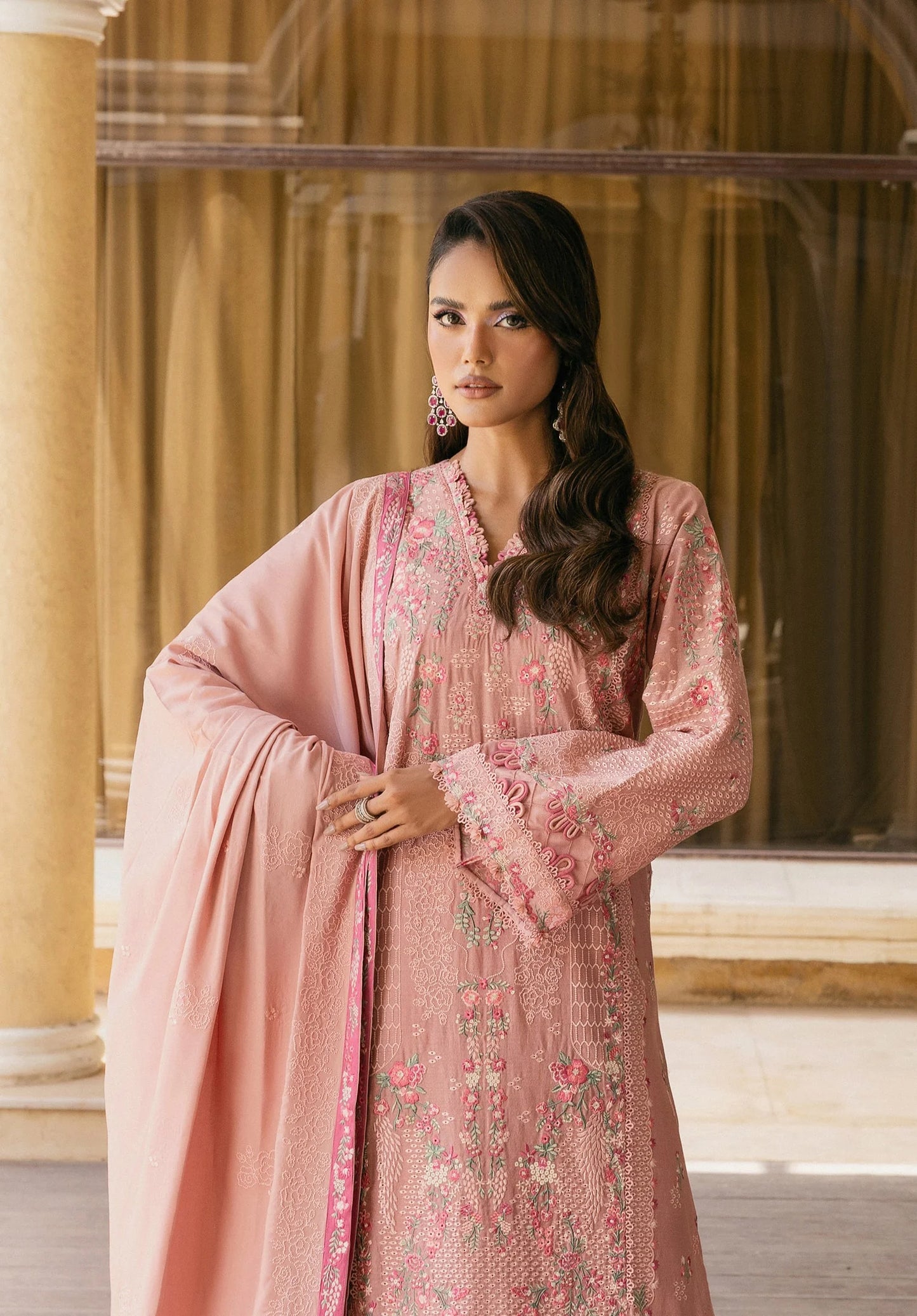 Woman wearing a pink embroidered outfit with a matching dupatta in an indoor setting.