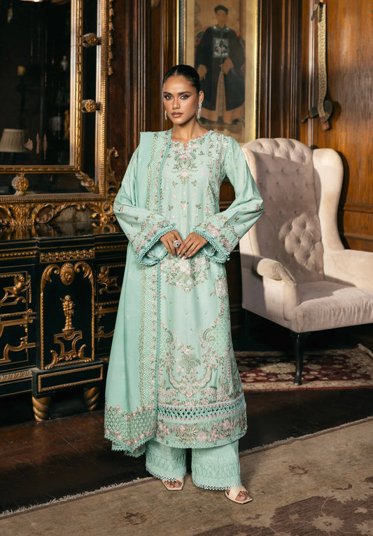 Woman in a light blue embroidered traditional outfit standing in an elegant room with a mirror and chair.