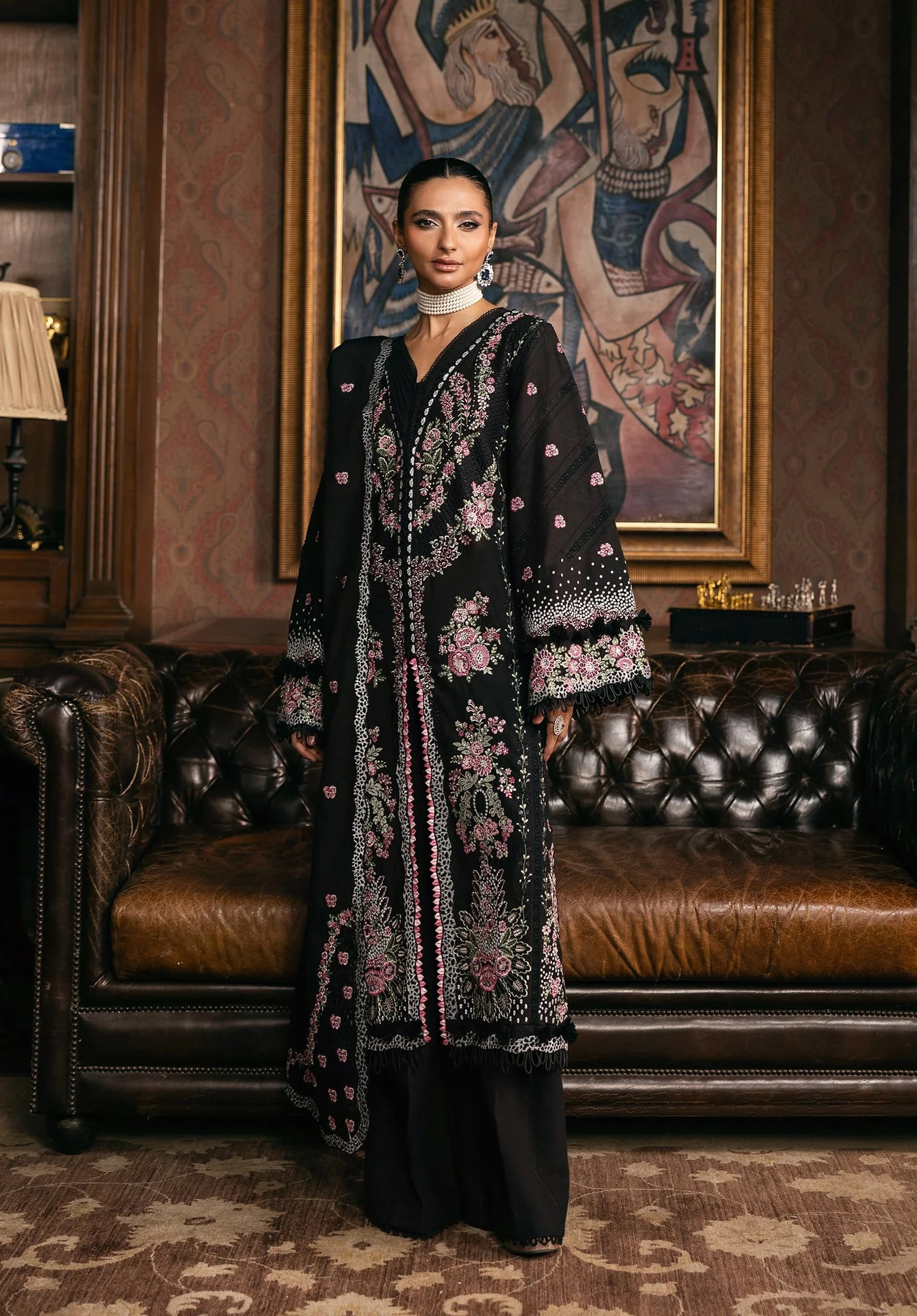 Woman in a black embroidered dress standing in an elegant room with a leather sofa and decorative wall art in ELAF LUXURY WINTER