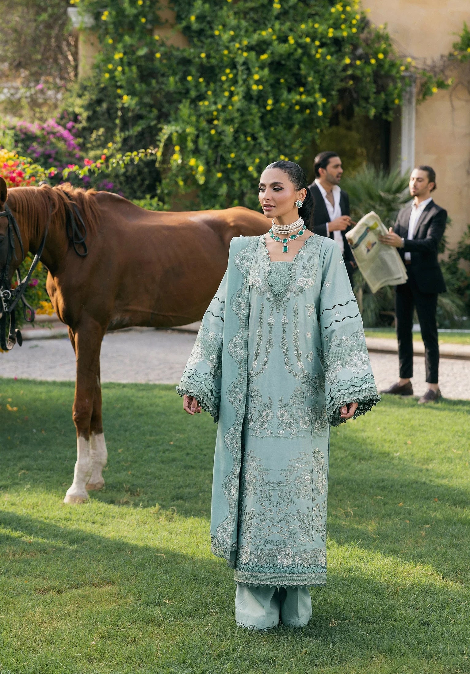 Woman in a light blue traditional outfit standing on grass with a horse in the background from elaf LUXURY WINTER '25