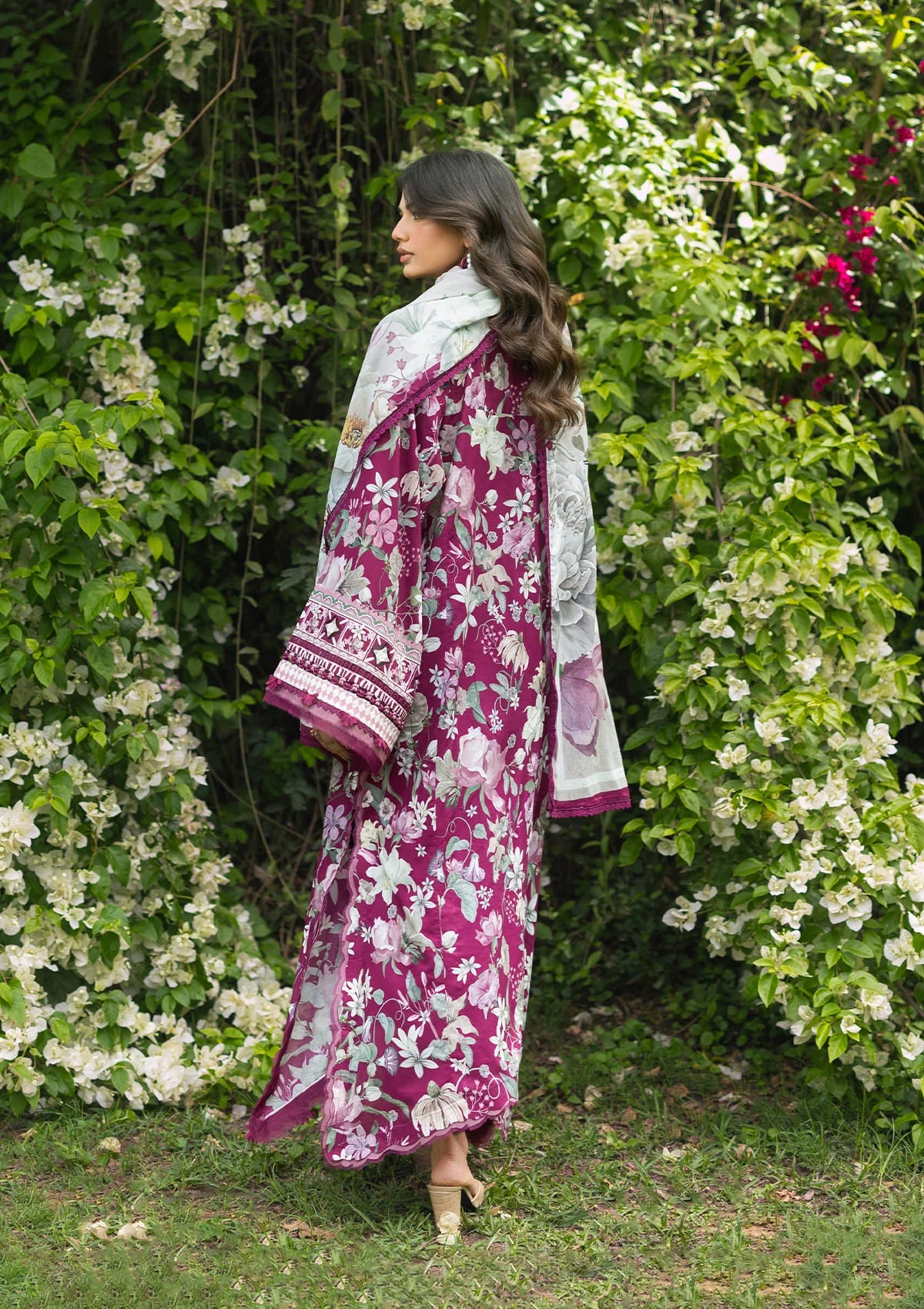 Woman wearing a floral dress with a pink border standing in front of green foliage.