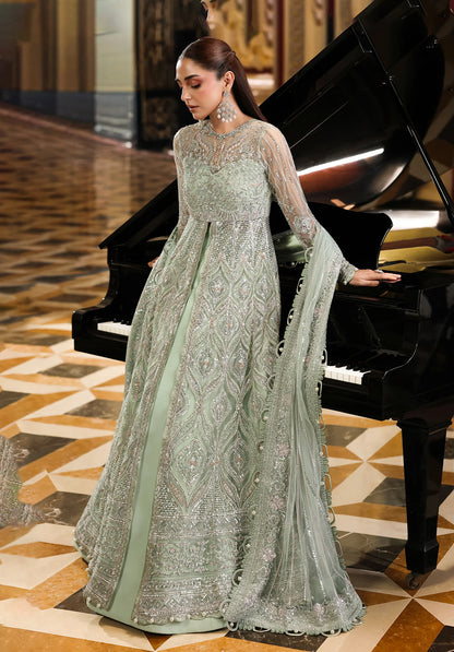 Woman in a light green embroidered dress standing next to a grand piano in an elegant interior setting.
