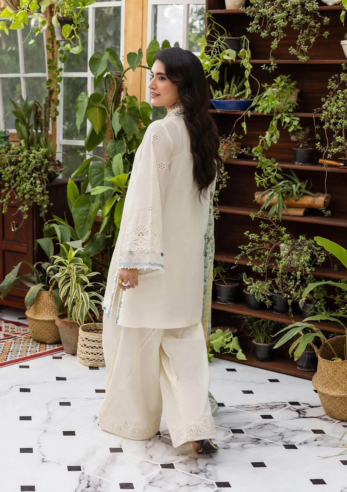 Woman in a white traditional outfit standing in a room with plants